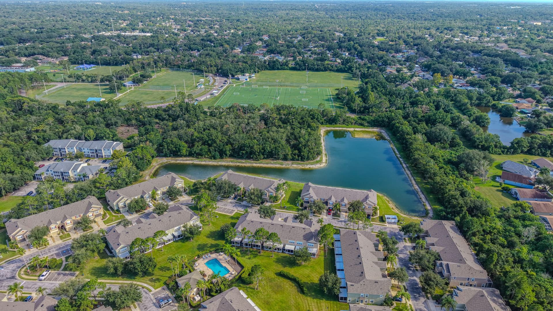Aerial view of a residential community with a pool, lake and sports fields