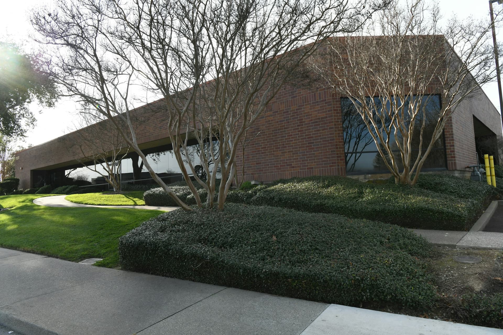 Single-story brick office building with mature trees and a landscaped lawn