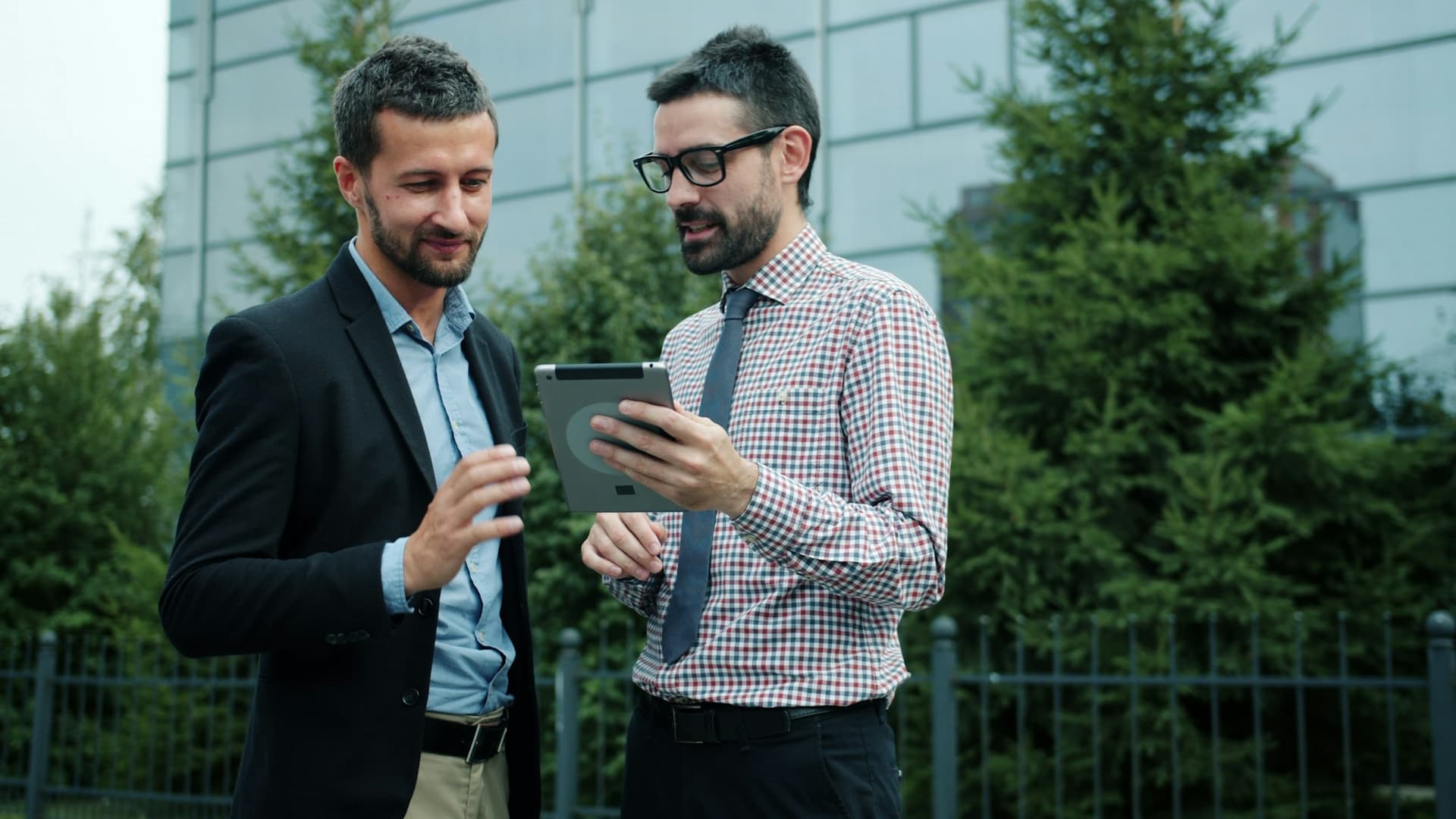Two people reviewing information on a tablet outside a glass office building