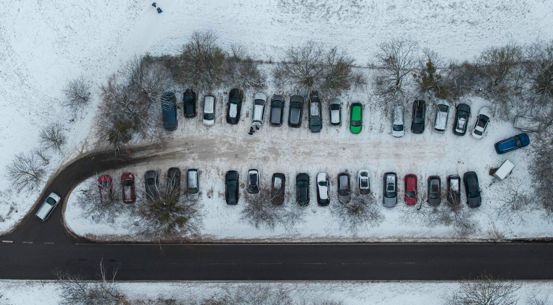 Aerial view of a snow-covered parking lot with plowed rows of cars